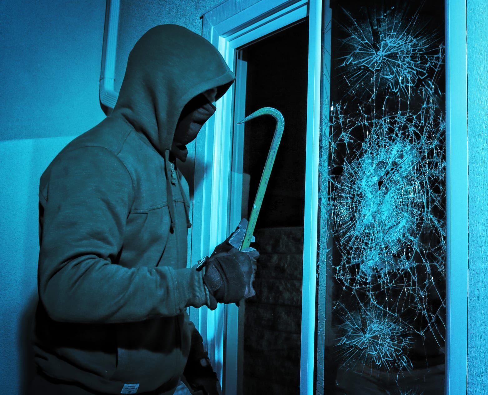 Burglar in a hook and mask attempting a break-in with shattered glass, highlighting the importance of security measures and window protection for businesses. Ideal for crime prevention and security-focused content.